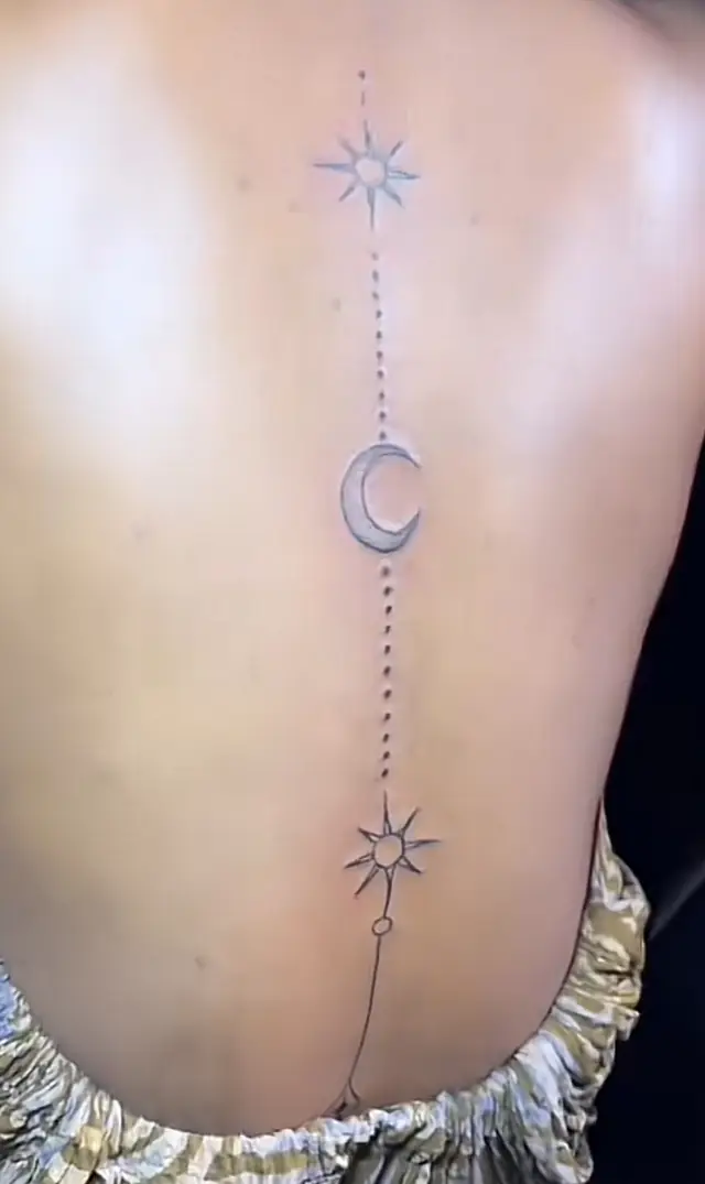 Fine-line spine tattoo of two sun motifs and a crescent moon joined by a dotted line